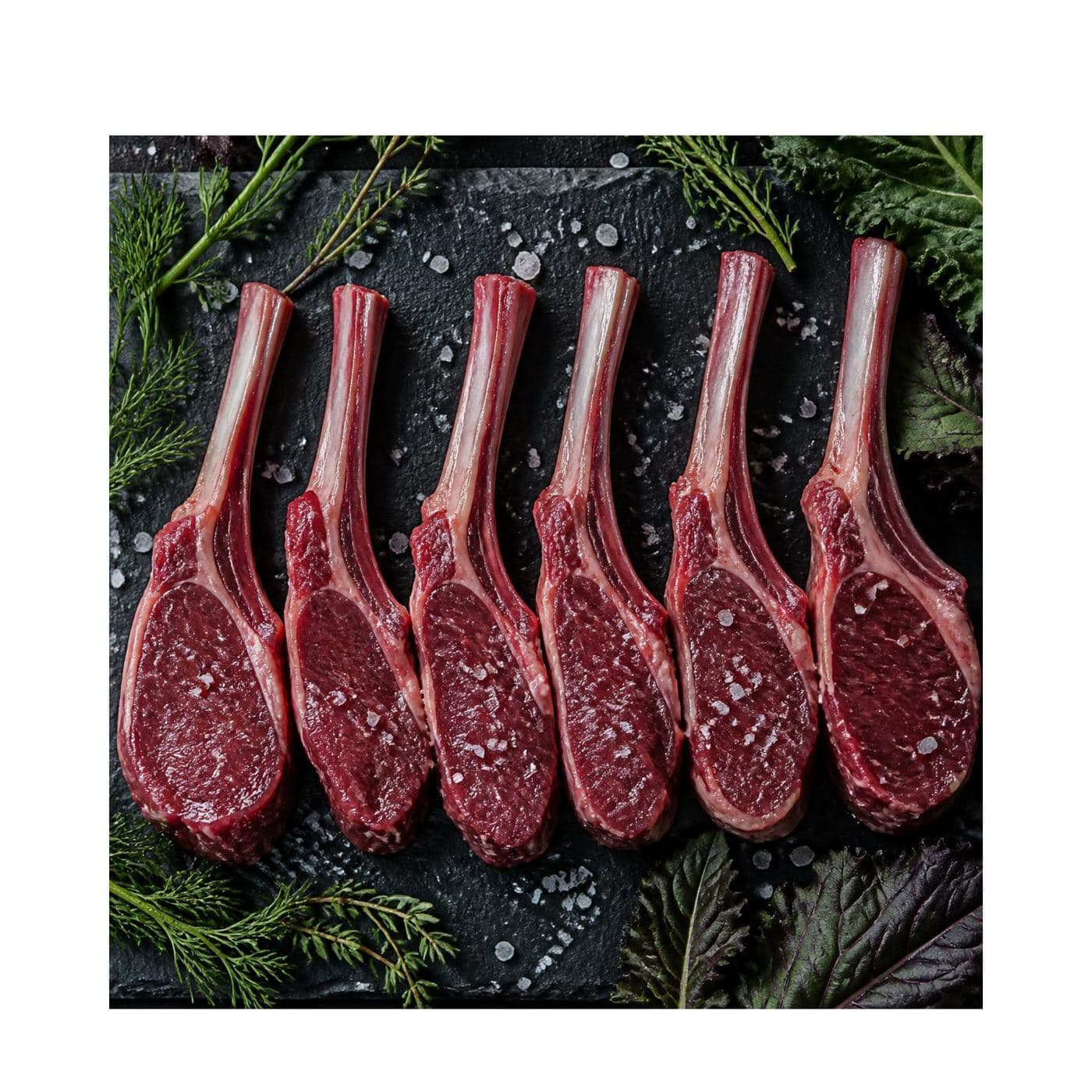 Trimmed organic venison cutlets arranged on a dark slate board with fresh herbs and sea salt