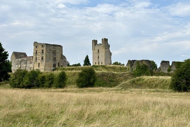 The ruins of Helmsley Castle rising above trees and a grass bank in North Yorkshire